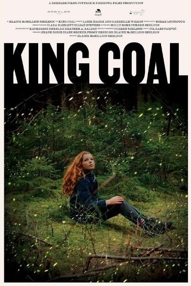 A person sitting on grass in the woods surrounded by shrubs with large text saying King Coal
