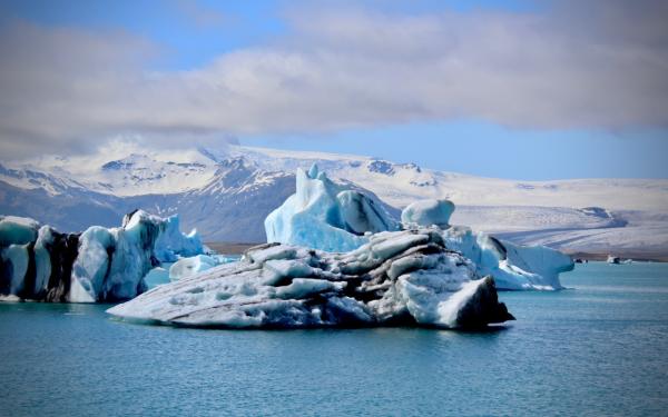 Heavily eroded icebergs floating in a bay surrounded by mountains