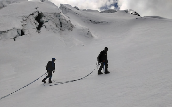 2 people in snow covered field hiking up a mountain, tethered to each other.