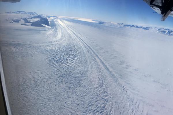Image of snow covered ground from a plane with part of the plane in the right side of the image.