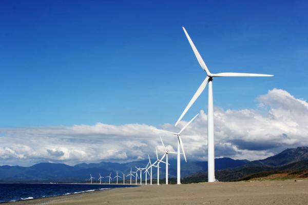 White wind turbines on sand near body of water under blue skies with white clouds.